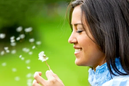 Schöne Frau bläst eine Blume und lächelt